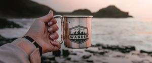Preview wallpaper mug, hand, water, rocks, sunset