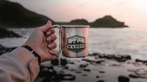 Preview wallpaper mug, hand, water, rocks, sunset