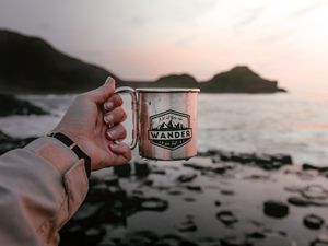 Preview wallpaper mug, hand, water, rocks, sunset