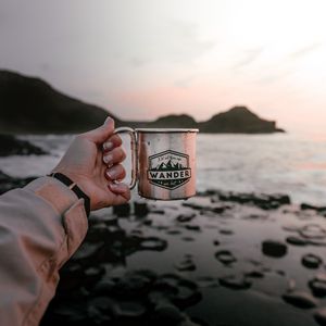Preview wallpaper mug, hand, water, rocks, sunset