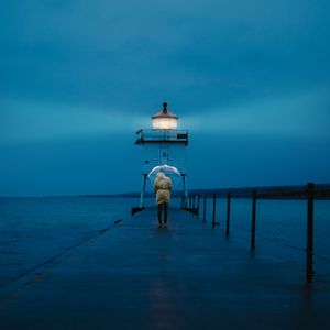 Preview wallpaper pier, man, lighthouse, umbrella, sea, twilight