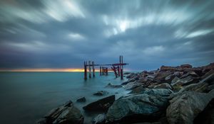 Preview wallpaper pilings, sea, stones, shore, sunset