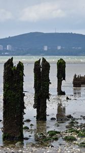 Preview wallpaper pilings, shore, pebbles, sea, mountains