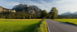 Preview wallpaper road, asphalt, field, green, trees, mountains, castle