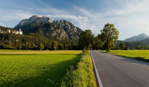 Preview wallpaper road, asphalt, field, green, trees, mountains, castle