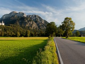 Preview wallpaper road, asphalt, field, green, trees, mountains, castle