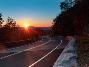 Preview wallpaper road, turn, trees, rays, sunset