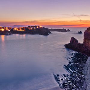 Preview wallpaper rocks, moon, sea, sky, decline, coast, city, fires, twilight, pebble