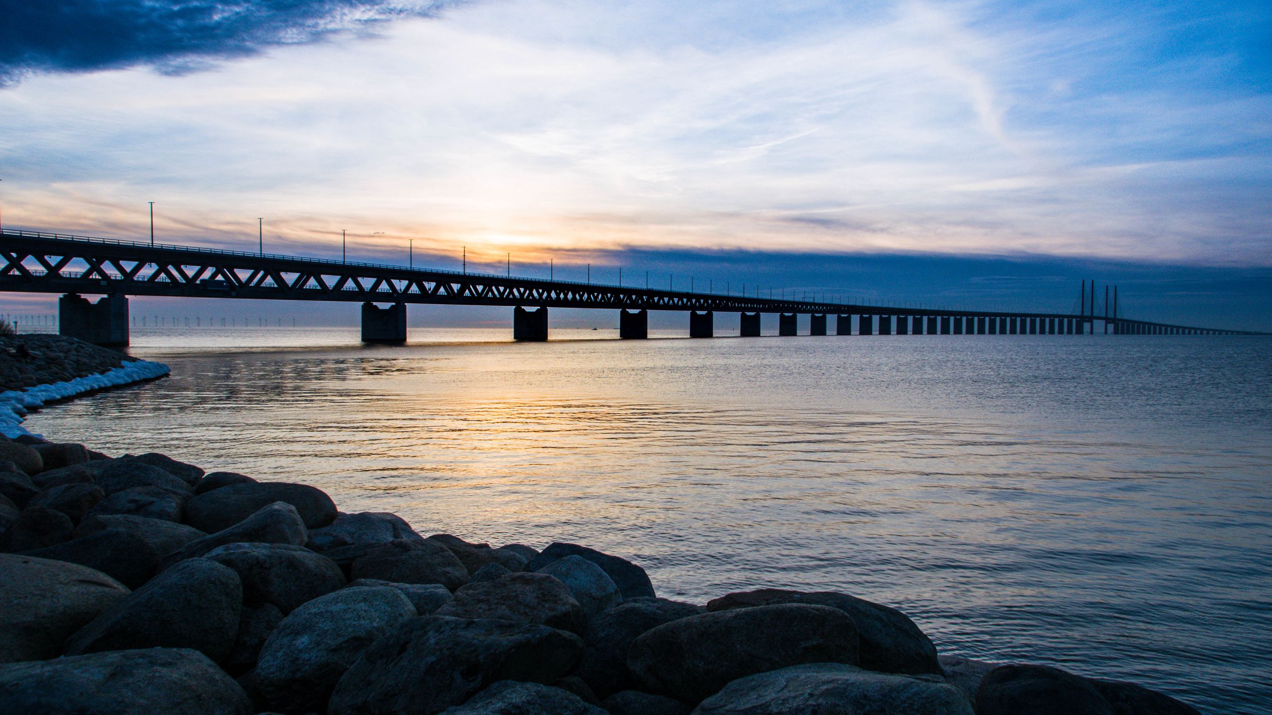 Download wallpaper 2560x1440 sea, bridge, coast, stones, sunset