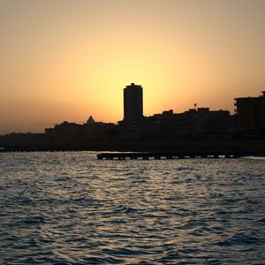 Preview wallpaper sea, pier, buildings, city, silhouettes, evening