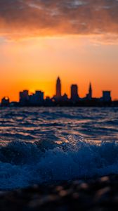 Preview wallpaper sea, waves, city, buildings, silhouettes, sunset