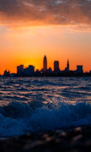 Preview wallpaper sea, waves, city, buildings, silhouettes, sunset