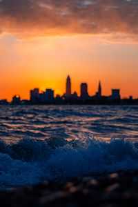 Preview wallpaper sea, waves, city, buildings, silhouettes, sunset