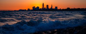 Preview wallpaper sea, waves, city, buildings, silhouettes, sunset