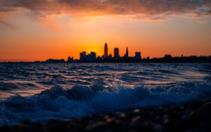 Preview wallpaper sea, waves, city, buildings, silhouettes, sunset