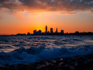 Preview wallpaper sea, waves, city, buildings, silhouettes, sunset