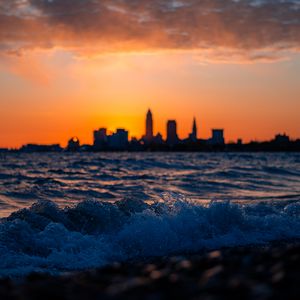 Preview wallpaper sea, waves, city, buildings, silhouettes, sunset