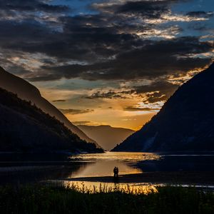 Preview wallpaper silhouettes, couple, mountains, lake, sunset, clouds, norway