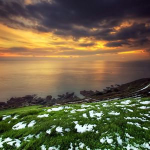 Preview wallpaper snow, grass, green, coast, sea, clouds, sky, orange, decline, anomaly