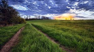 Preview wallpaper sun, light, beams, grass, field, road, traces, clouds, layer, evening, orange