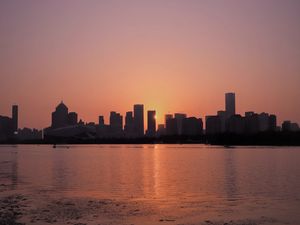 Preview wallpaper sunset, city, building, rays, sea