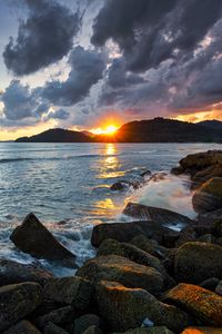 Preview wallpaper sunset, rays, coast, sea, stones