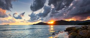 Preview wallpaper sunset, rays, coast, sea, stones