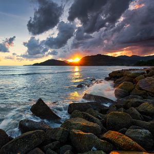 Preview wallpaper sunset, rays, coast, sea, stones