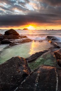 Preview wallpaper sunset, rays, stones, sea, rocks