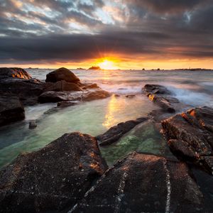 Preview wallpaper sunset, rays, stones, sea, rocks