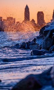 Preview wallpaper water, waves, spray, stones, city, sunset