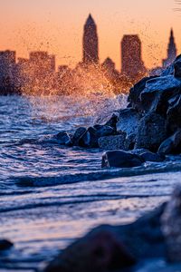 Preview wallpaper water, waves, spray, stones, city, sunset