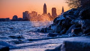 Preview wallpaper water, waves, spray, stones, city, sunset