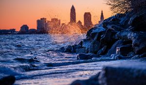 Preview wallpaper water, waves, spray, stones, city, sunset