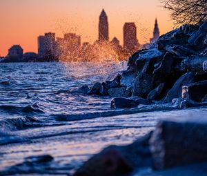 Preview wallpaper water, waves, spray, stones, city, sunset