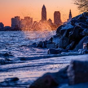 Preview wallpaper water, waves, spray, stones, city, sunset